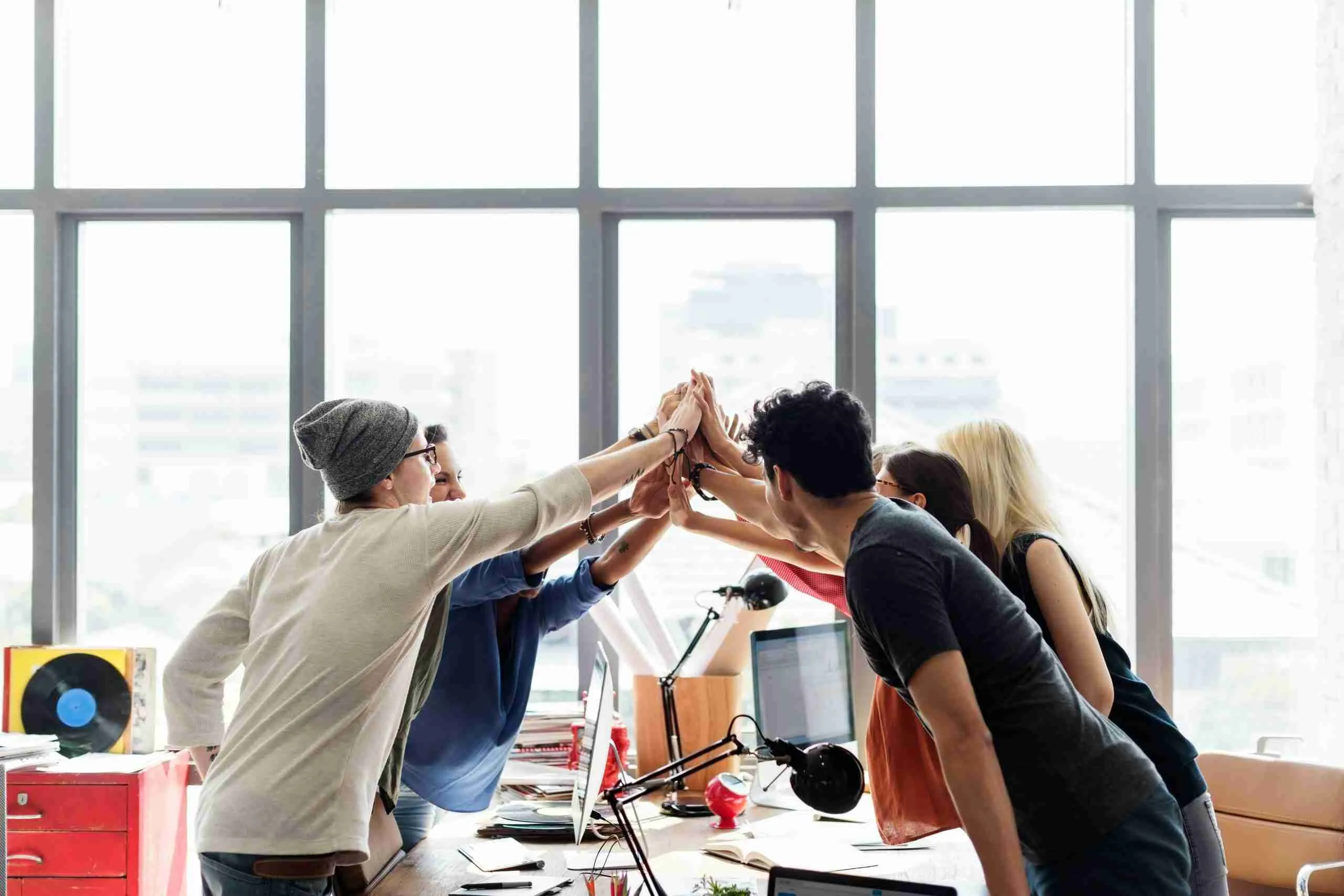 getty-images-WnZegqeK-vk-unsplash A group of coworkers in a bright office celebrating by forming a circle and high-fiving each other.